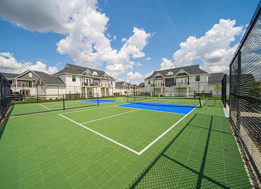 A tennis court surrounded by a fence and apartment buildings.