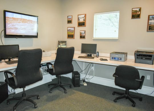 a computer room with three desks and three chairs and a monitor