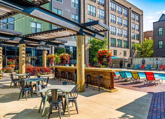 a patio with tables and chairs next to a pool with a building in the background
