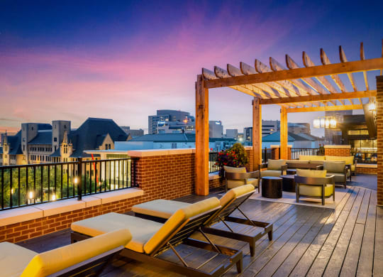 a rooftop deck with lounge chairs and a pergola at sunset