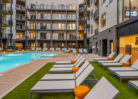 A pool area with sun loungers and apartment buildings in the background.
