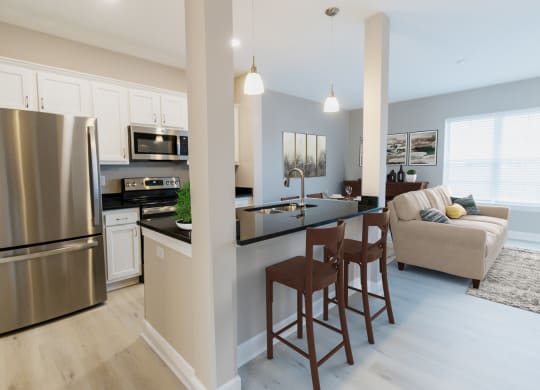 a kitchen and living room with stainless steel appliances and a bar with stools