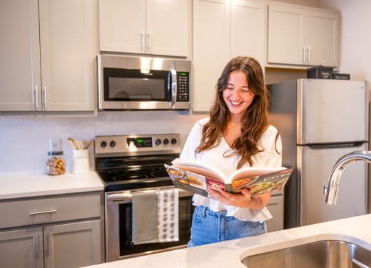 a woman standing in a kitchen reading a magazine