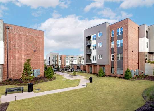 A modern apartment complex with a grassy courtyard and a bench.
