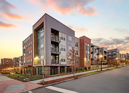 Apartment buildings are shown in the evening with lights on.