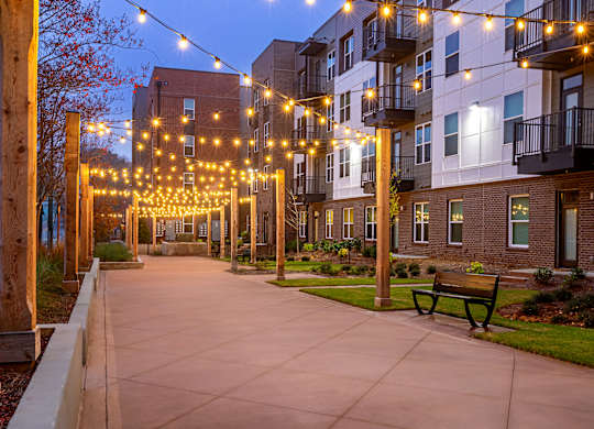 A walkway with a bench and lights leading to a building.