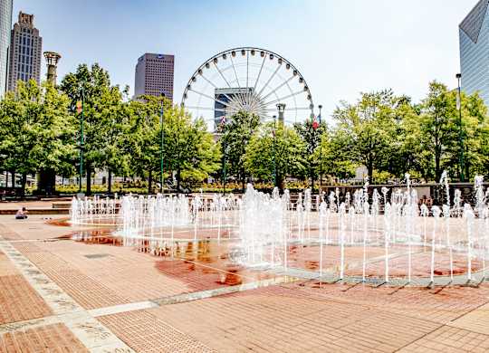 A fountain in the middle of a square with a Ferris wheel in the background.