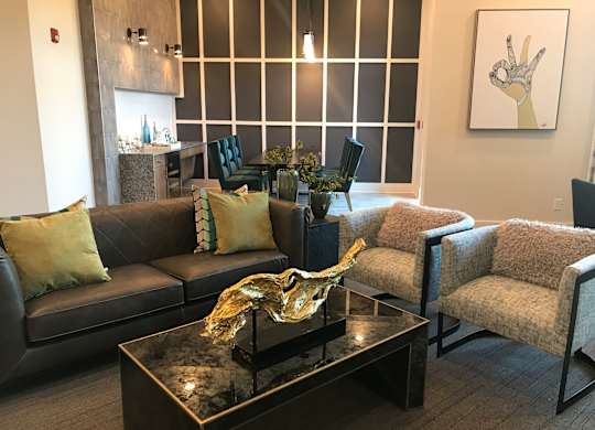A living room with a black couch, a coffee table, and a painting on the wall.
