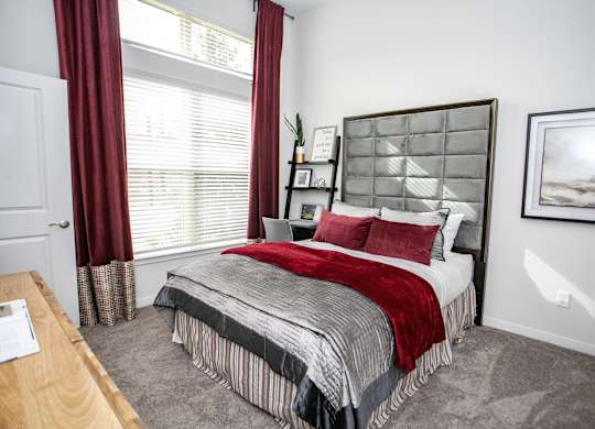 A bedroom with a bed, nightstand, and window with red curtains.