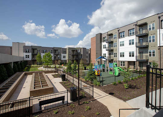 A playground area with a slide and a basketball court is located in front of apartment buildings.