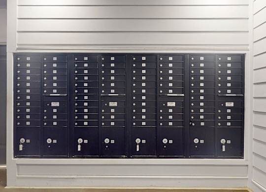 A row of black mailboxes are lined up on a wall.