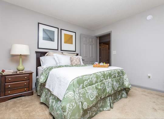 A bedroom with a bed, nightstand, lamp, and two pictures on the wall.