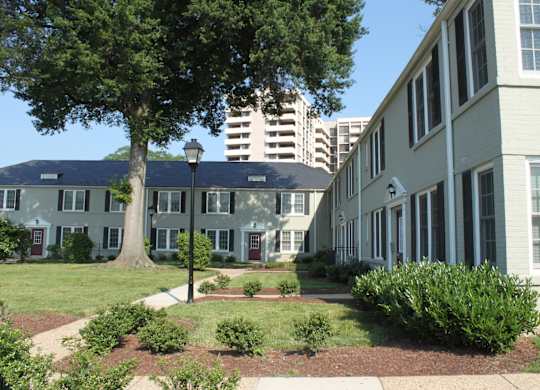 an exterior view of an apartment complex with a tree and a sidewalk