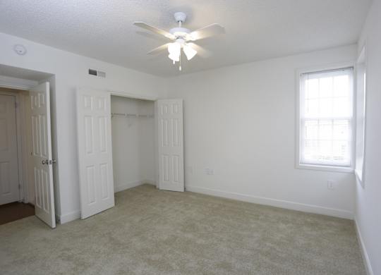an empty living room with a ceiling fan and a closet