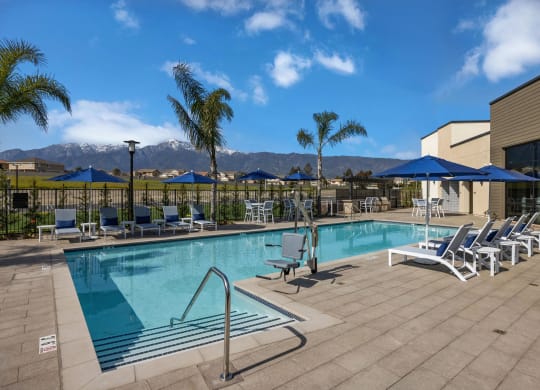 a swimming pool with chairs and umbrellas and mountains in the backgroundat Westbury Apartments, Rancho Cucamonga, California 