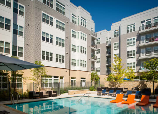 a swimming pool with orange chairs in front of an apartment building at The Metropolitan Downtown Columbia, Columbia, 21044