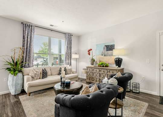 A living room with a grey armchair, a white sofa, a wooden coffee table, and a white vase with a green plant.
