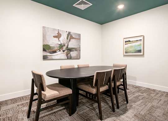 A conference room with a table and chairs and two pictures on the wall.