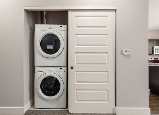 A white door is open to reveal a stacked washer and dryer.