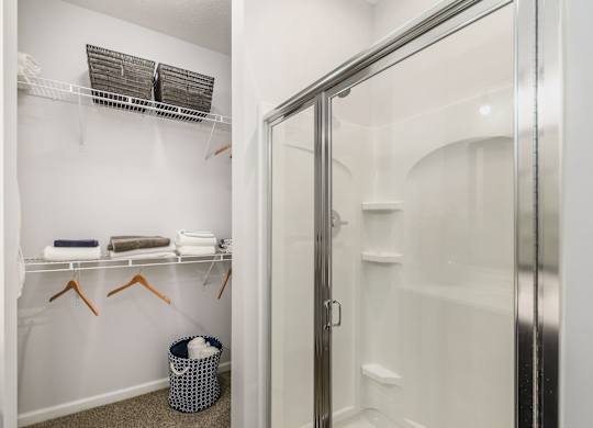 A bathroom with a white shower stall and a white towel rack with towels hanging on it.