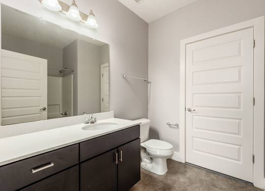 A white toilet sits in a bathroom with a white sink and a white door.