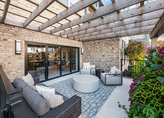 A patio with a black sofa, a round table and a stone wall.