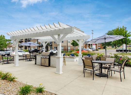 A white pergola with black chairs and tables is set up in a sunny outdoor area.