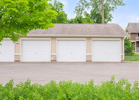 A two-car garage with a brown roof is surrounded by greenery.