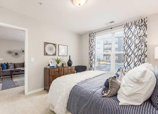 A bedroom with a bed, nightstand, and a window with a view of a building outside.