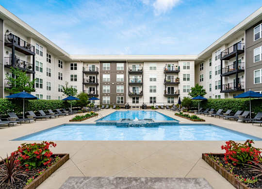 A large swimming pool is surrounded by a concrete patio and lounge chairs.
