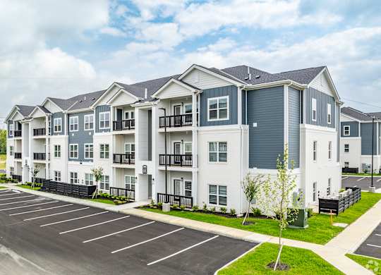 A large white apartment building with a parking lot in front.