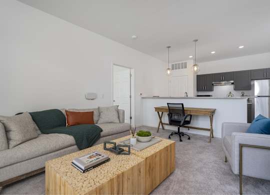 A living room with a couch, a coffee table, and a kitchen area in the background.