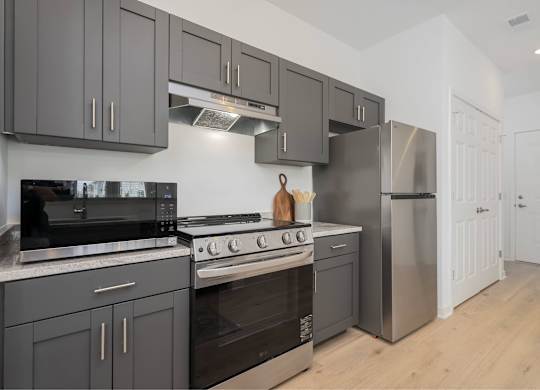 A modern kitchen with dark grey cabinets and stainless steel appliances.