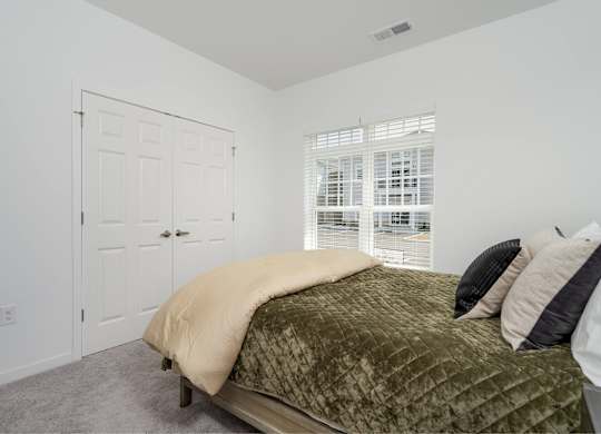 A bed with a green blanket and two pillows sits in a room with a window.