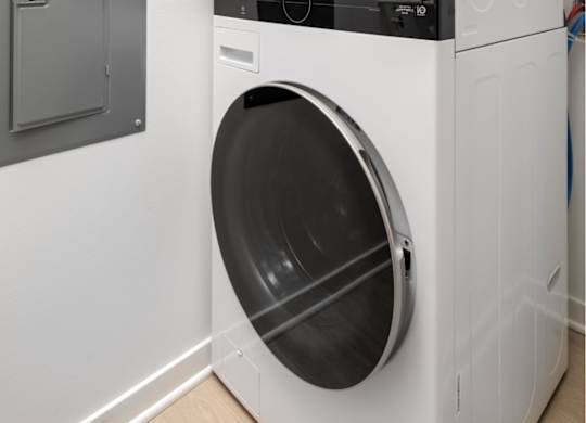 A white front load washing machine with a black door is next to a small storage cabinet.