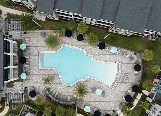 A swimming pool surrounded by a stone patio and umbrella tables.