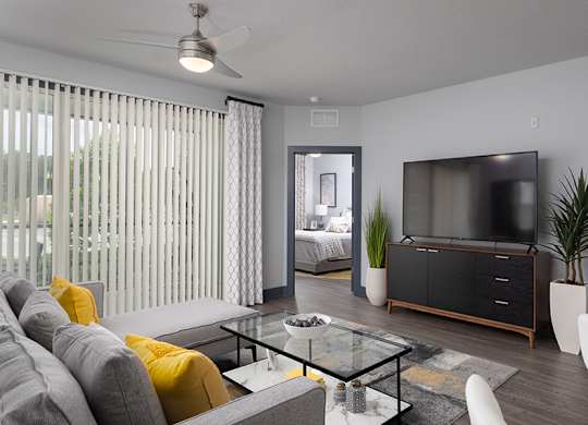 A modern living room with a grey sofa, a glass coffee table, and a flat screen TV.