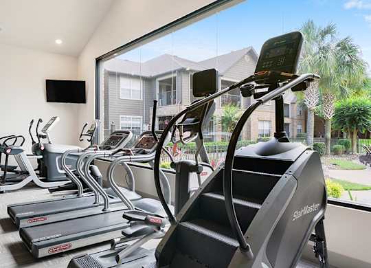 A row of treadmills in a gym with a view of a residential area outside the window.