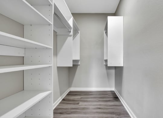 a walk in closet with white cabinets and a wooden floor