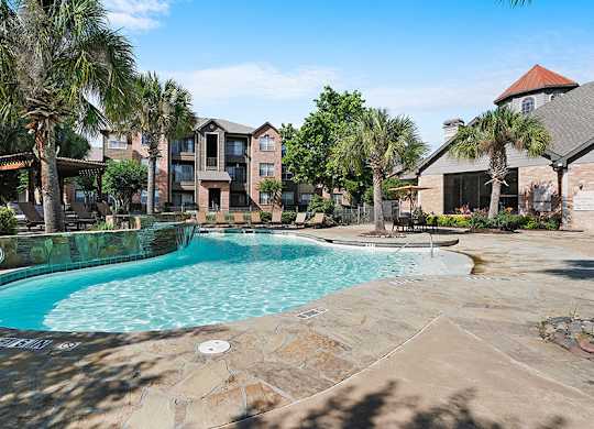 A swimming pool surrounded by palm trees and a building in the background.
