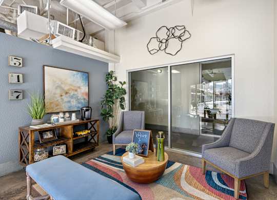 A modern living room with a grey sofa, a grey armchair, a wooden coffee table, and a large painting on the wall.