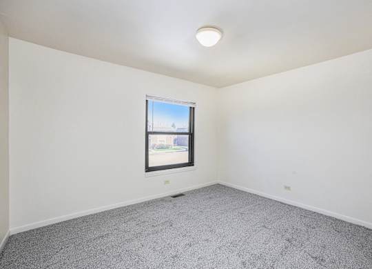 A room with a window and a grey carpet.