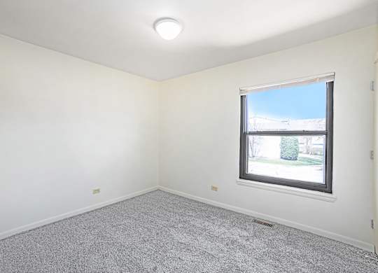 A room with a window and a grey carpet.