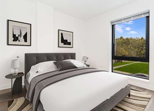 A bedroom with a large bed and a view of a green lawn outside the window.