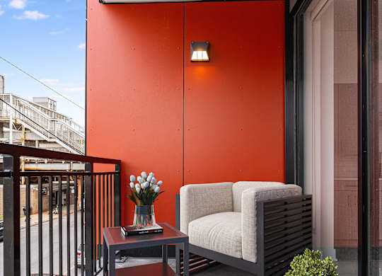 A small balcony with a table, a sofa, and a potted plant.