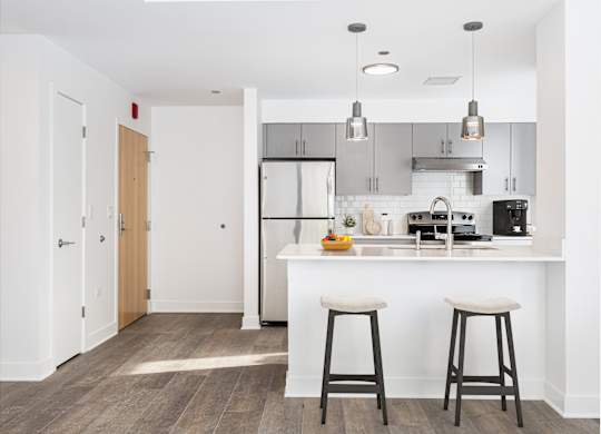 A kitchen with white countertops and bar stools.