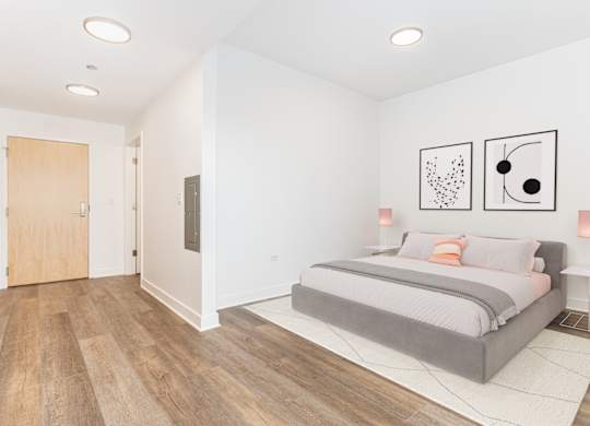 A bedroom with a bed, two pictures on the wall, and a wooden floor.