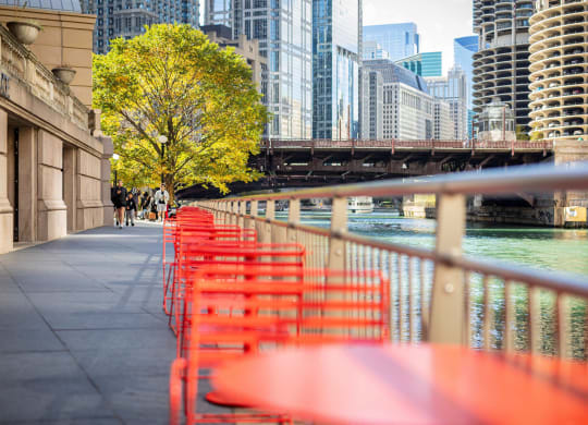 a row of red tables and chairs next to the river in a city