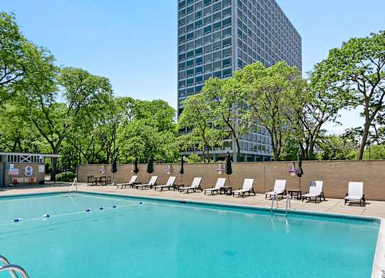 A swimming pool surrounded by trees and chairs with a building in the background at The Pavilion, Detroit, MI, 48207