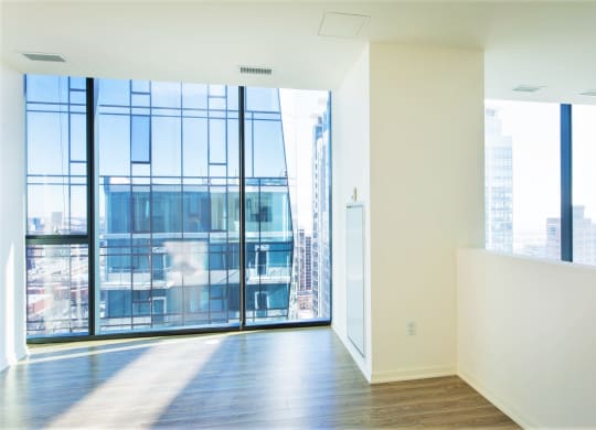an empty room with white walls and floor to ceiling windows with a view of the city